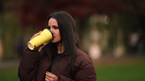Portrait-of-Beautiful-Young-Brunette-Girl-Model-Holding-and-Drinking-Coffee-Cup-in-Outdoor-Park,-Blurred-Background