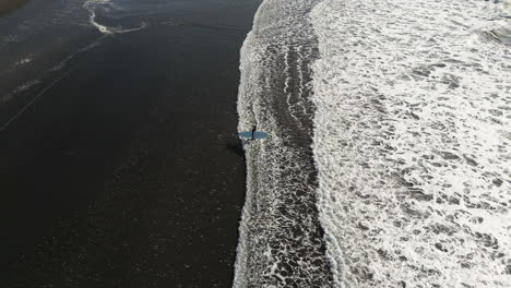 drone-view-of-a-surfer-who-enters-the-water,-side-view