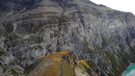 A-spinning-aerial-view-of-cliff-viewpoint-of-lake-Limmernsee-in-Glarus,-Switzerland,-with-hikers-enjoying-the-view-of-the-Swiss-Alps-cliffs,-landscape-and-turquoise-water