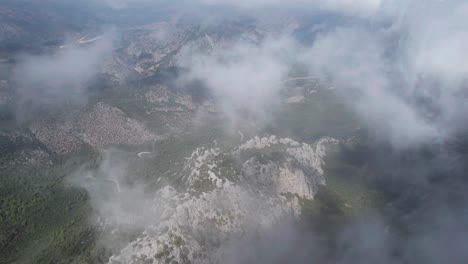 AERIAL-drone-over-clouds-and-mountains-on-the-valley-of-Termessos,-Turkey,-forward-tilt-down