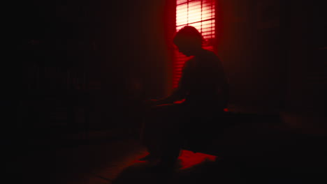 Woman-sits-on-sofa-as-red-light-silhouettes-her-from-window
