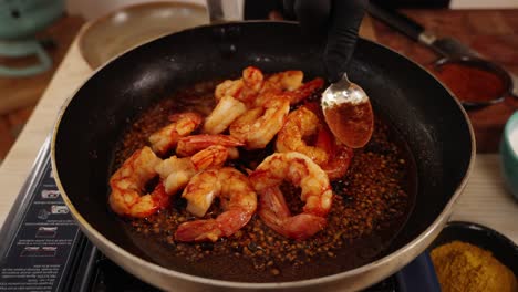 Chef-crushing-the-garlics-in-the-boiling-oil-on-the-cooking-pan-with-a-spoon-to-infused-the-flavours-in-the-sauteed-seafood-prawn-dish,-close-up-shot
