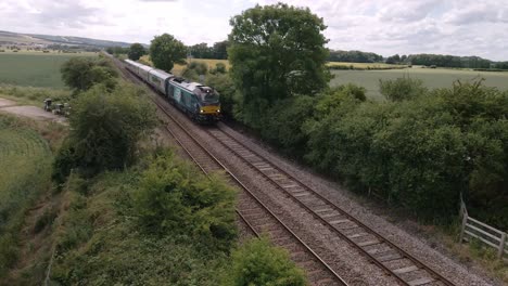 low-angle-Aerial-view-of-a-passenger-train-driving-on-tracks-in-the-countryside-in-England