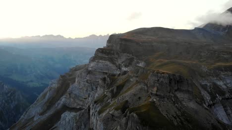 Eine-Sich-Drehende-Luftaufnahme-Von-Muttenchopf-Aussichtspunkt-Des-Limmernsees-In-Glarus,-Schweiz,-Mit-Den-Schweizer-Alpen,-Klippen,-Blauem-Wasser,-Wanderern-Im-Blick-Nach-Einem-Sonnenuntergang