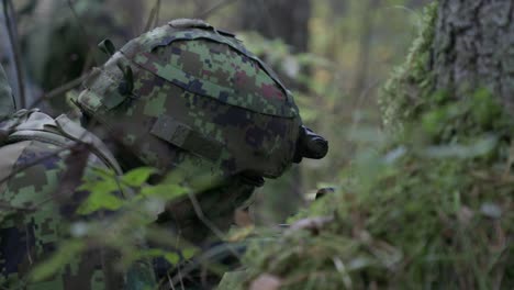 Soldier-lying-down-stalking-in-forest-aiming-rifle,-handheld,-closeup,-slow-motion