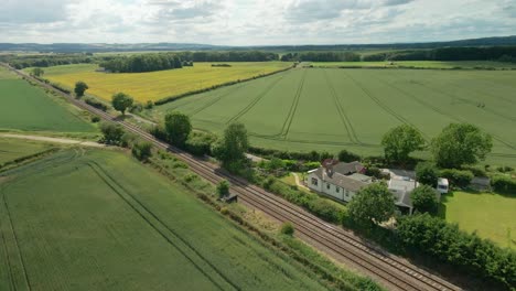 Aerial-view-of-British-rural-scene-with-train-tracks,-agricultural-farmland-and-green-fields