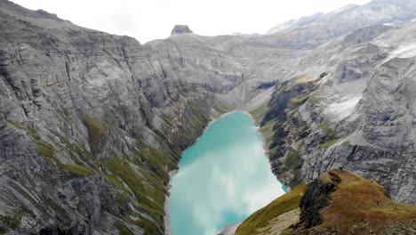 A-flyover-above-a-viewpoint-of-lake-Limmernsee-in-Glarus,-Switzerland,-with-hikers-enjoying-the-view-of-the-Swiss-Alps-cliffs,-landscape-and-turquoise-water