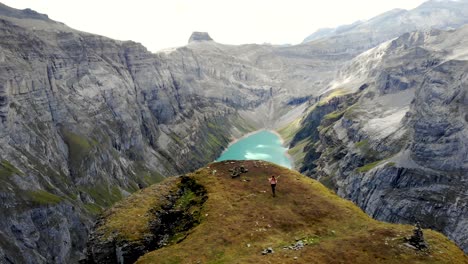 A-hiker-running-towards-the-viewpoint-of-lake-Limmernsee-in-Glarus,-Switzerland,-the-turquoise-colored-water-of-which-is-surrounded-by-tall-Swiss-Alps-peaks-and-cliffs