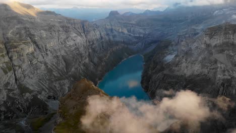 A-flyover-above-lake-Limmernsee-in-Glarus,-Switzerland,-with-view-of-sunlit-glowing-clouds,-a-hydroelectric-dam-and-reservoir-surrounded-by-cliffs-after-sunset