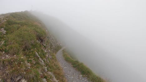 Hiking-man-walks-out-of-the-thick-fog-on-narrow-trail-in-Alps,-Switzerland