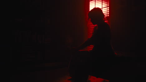 Woman-sits-on-sofa-as-red-light-silhouettes-her-from-window