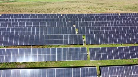 Sun-shinning-on-blue-color-solar-panel-cells-in-green-meadow,-aerial-view
