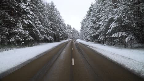 POV-of-car-driving-on-snowy-frosty-asphalt-road-surrounded-by-snow-covered-pine-trees-in-winter
