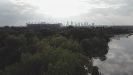 Aerial-drone-shot-of-warsaw-skyline-with-national-stadium,-forest,-lake-on-a-sunny-day