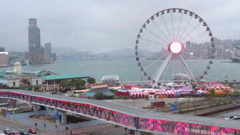 A-pedestrian-bridge-is-decorated-with-Chinese-red-lanterns-as-people-walk-through-it-while,-in-the-background,-there-is-a-Ferris-wheel-in-Hong-Kong