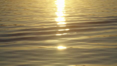 Golden-sunlight-reflection-glimmering-on-ocean-surface,-waves-rippling