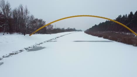 Drohnenvideo-Vom-Unterqueren-Einer-Gelben-Brücke-Auf-Einem-Zugefrorenen-Fluss-Im-Wald-In-Warschau