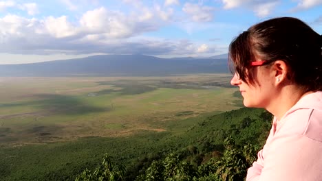 Woman-with-glasses-turns-head-smiles-with-volcanic-landscape-of-Ngorongoro-in-background