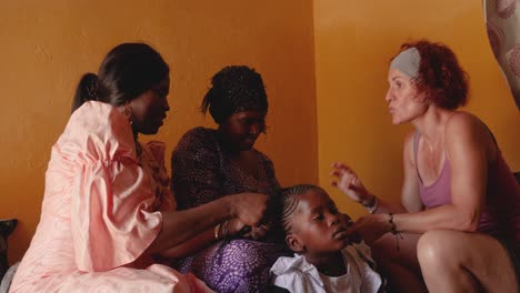 Two-black-women-and-a-white-woman-make-braids-on-the-head-of-a-young-african-girl,-inside-a-Mauritanian-house
