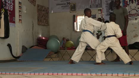 Dos-Niños-Africanos-Entrenan-Karate-A-Un-Lado-De-Su-Sensei-Dentro-De-Un-Dojo-En-Nouakchott,-Mauritania
