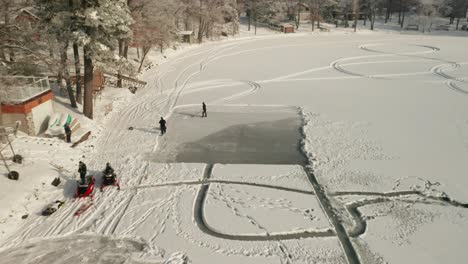 Aerial,-workers-clearing-snow-on-a-frozen-lake-to-create-ice-rink