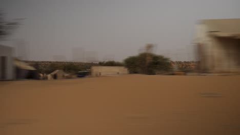 Eine-Aufnahme-Der-Senegalesischen-Landschaft,-Aufgenommen-Aus-Einem-Auto,-Mit-Einigen-Häusern,-Bäumen-Und-Viel-Sand