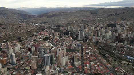 Aerial-Drone-Fly-Above-La-Paz,-Bolivia,-Stadium-Hernando-Siles,-Crowder-Metropolitan-City,-Houses,-Skyscrapers-and-Andean-Cordillera-Mountain-Range-in-the-Background