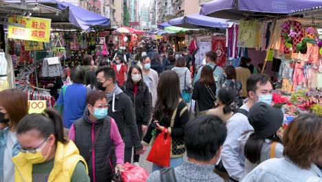 People-walk-through-an-outdoor-crowded-street-stall-market-as-they-look-for-bargain-priced-vegetables,-fruits,-gifts,-and-fashion-goods-in-Hong-Kong
