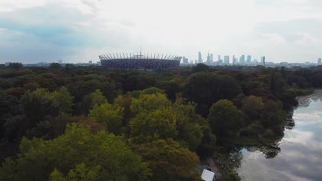 Aerial-drone-video-of-national-stadium-of-warsaw-with-city-view,-forest-and-lake-in-the-background