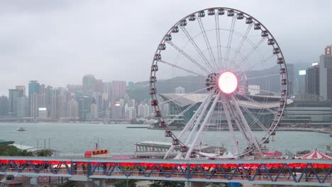 A-pedestrian-bridge-is-decorated-with-Chinese-red-lanterns-as-people-walk-through-it-while,-in-the-background,-there-is-a-Ferris-wheel-in-Hong-Kong