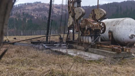 Old-and-rusty-oil-drilling-equipment-with-storage-tank-in-a-field-with-mountains-in-the-distance