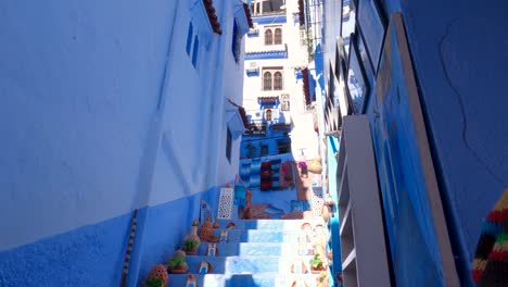 View-Looking-Up-At-Tall-Blue-Apartments-Chefchaouen-With-Tilt-Down-To-Decorative-Pots-On-Steps