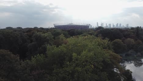 Establishing-drone-shot-of-warsaw-stadium-with-city-skyline-and-forest-in-the-background