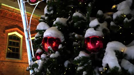 Nahaufnahmeaufnahme-Eines-Mit-Roten-Spielzeugen-Geschmückten-Weihnachtsbaums,-Der-Nachts-In-Raudondvaris,-Litauen,-Mit-Schnee-Bedeckt-Ist