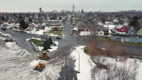 Residential-neighborhood-with-Heavy-equipment-removing-and-cleaning-Snow-from-Snowstorm,-Aerial-Dolly-shot
