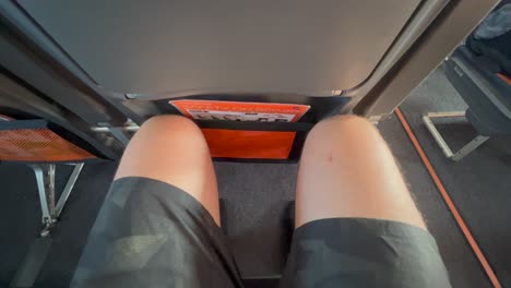 Traveling-in-tight-airplane-seat-with-very-little-legroom-in-Easyjet-airlines,-male-legs-and-knees-squeezed-tight-on-an-Easyjet-aircraft,-uncomfortable-seat,-4K-shot