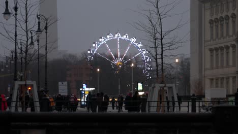 Glowing-Ferris-wheel-in-Berlin-city-downtown,-people-walk-in-foreground
