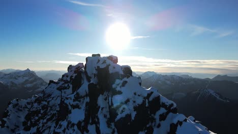 Ascending-drone-shot-of-bright-sun-behind-snowy-peak-of-mountain-in-Norway---beautiful-mountain-landscape-in-winter