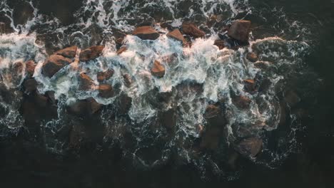 Aerial-top-down,-ocean-wave-crashing-into-rocks-creating-foam