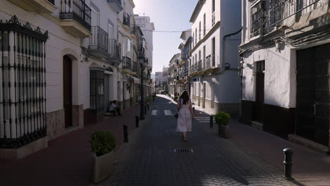 Vista-Trasera-De-Una-Chica-Con-Vestido-Blanco-Paseando-Por-Las-Calles-Vacías-De-Olvera,-España