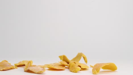 Dehydrated-dried-mango-pieces-falling-onto-white-table-top-and-bouncing-and-landing-in-a-pile-in-slow-motion