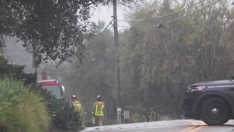 Zwei-Feuerwehrleute-Laufen-Im-Regen-Mit-Einem-Streifenwagen,-Der-Die-Straße-Blockiert