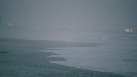 Calm-ocean-tide-rolling-onto-shore,-misty-overcast-dawn-dusk-evening