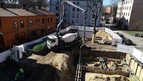 Concrete-vehicle-pour-cement-with-long-arm-in-construction-site,-aerial-view