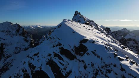 Luftaufnahme-Von-Schneebedeckten-Bergen-In-Norwegen-Mit-Eisigem-Gipfel-Und-Blauem-Himmel-Im-Winter