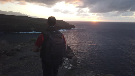 mature-man-with-backpack-on-his-back-walks-along-the-cliffs-of-the-coast-of-the-municipality-of-Galdar-during-sunset
