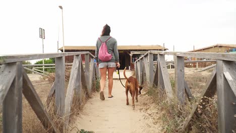 Woman-Walking-With-Boxer-Dog-In-Rural-Path-Near-Beach,-Spain,-Europe