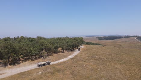 Israel-Army-squad-soldiers-on-vehicles-driving-through-green-field-at-training-ground-country-road,-Aerial-Tracking-shot