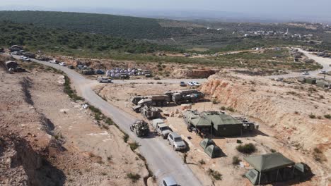 Israel-Army-soldiers-on-Humvee-vehicles-driving-through-training-ground-country-road,-Israeli-army-camping-area,-Aerial-shot