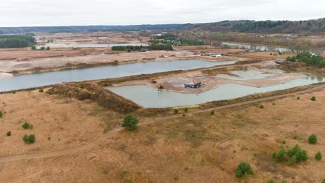 Water-pond-and-quarry-with-heavy-equipment,-aerial-drone-orbit-view